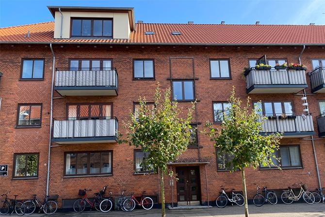 Klassisk rødmuret byejendom i København med altaner, kviste og cykler ved facaden