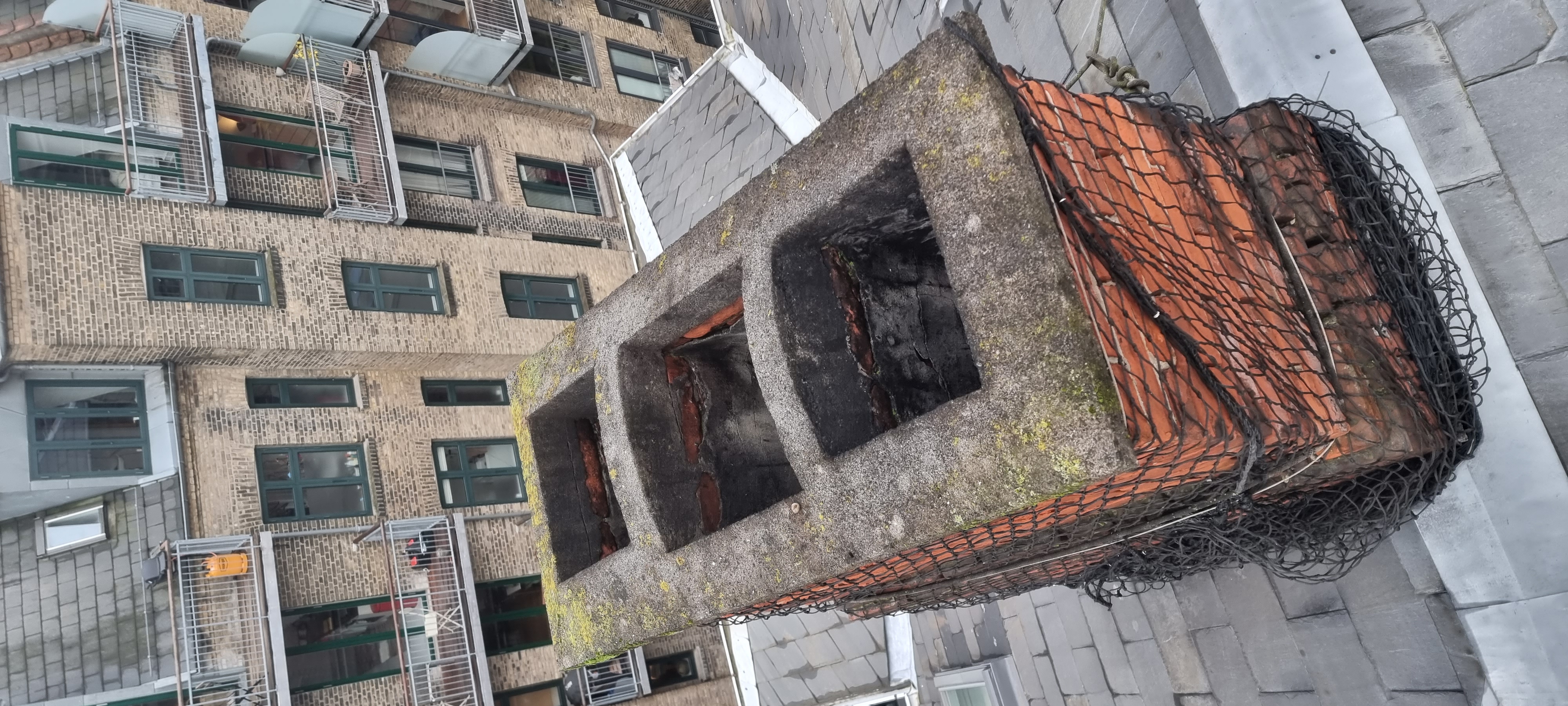 Drone nærbillede af sikkerhedsnet monteret på kritisk skorsten, mursten aktivt bag net
