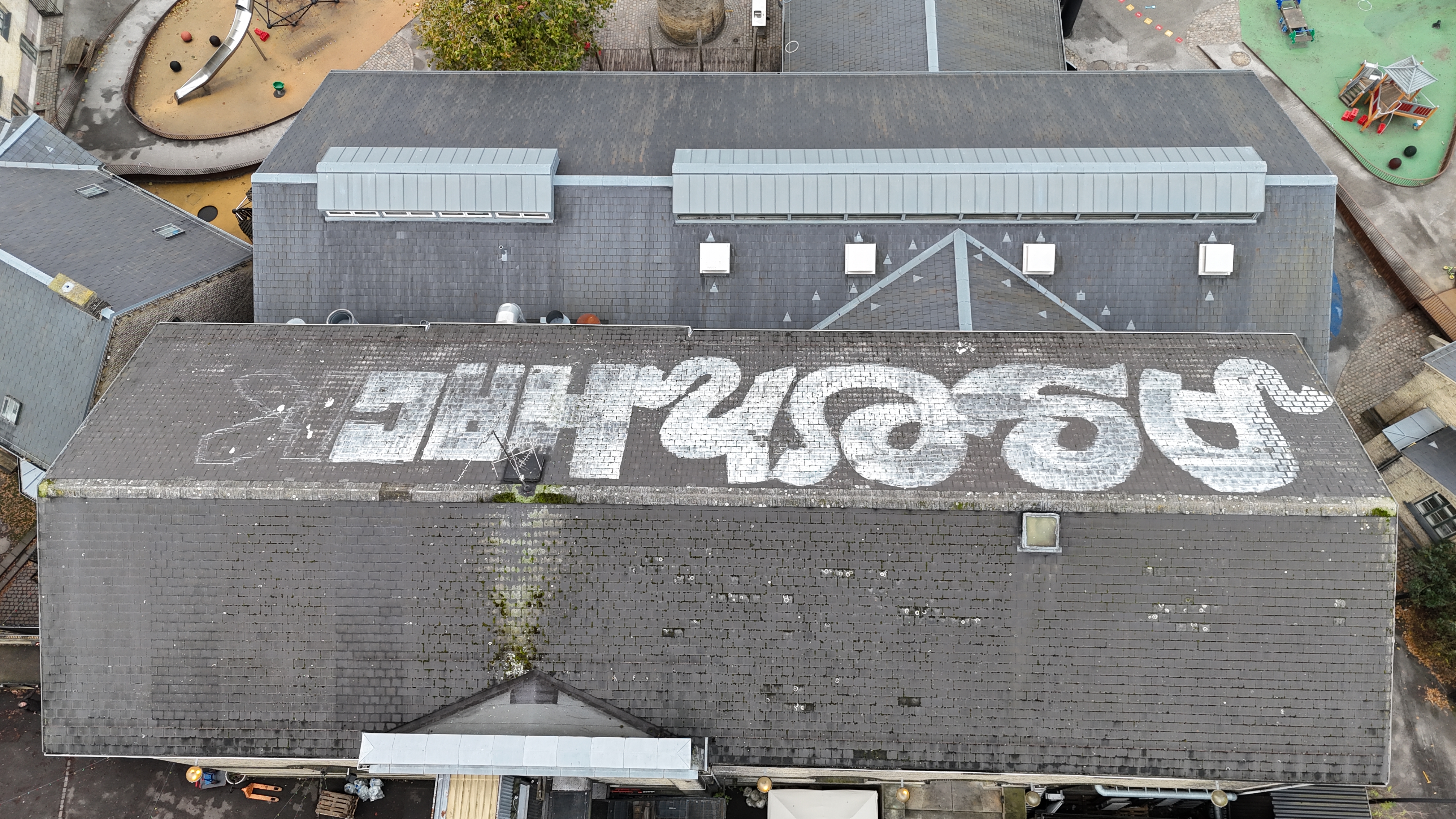 Drone overblik over to bygninger med skifertag, graffiti og mosbegroning