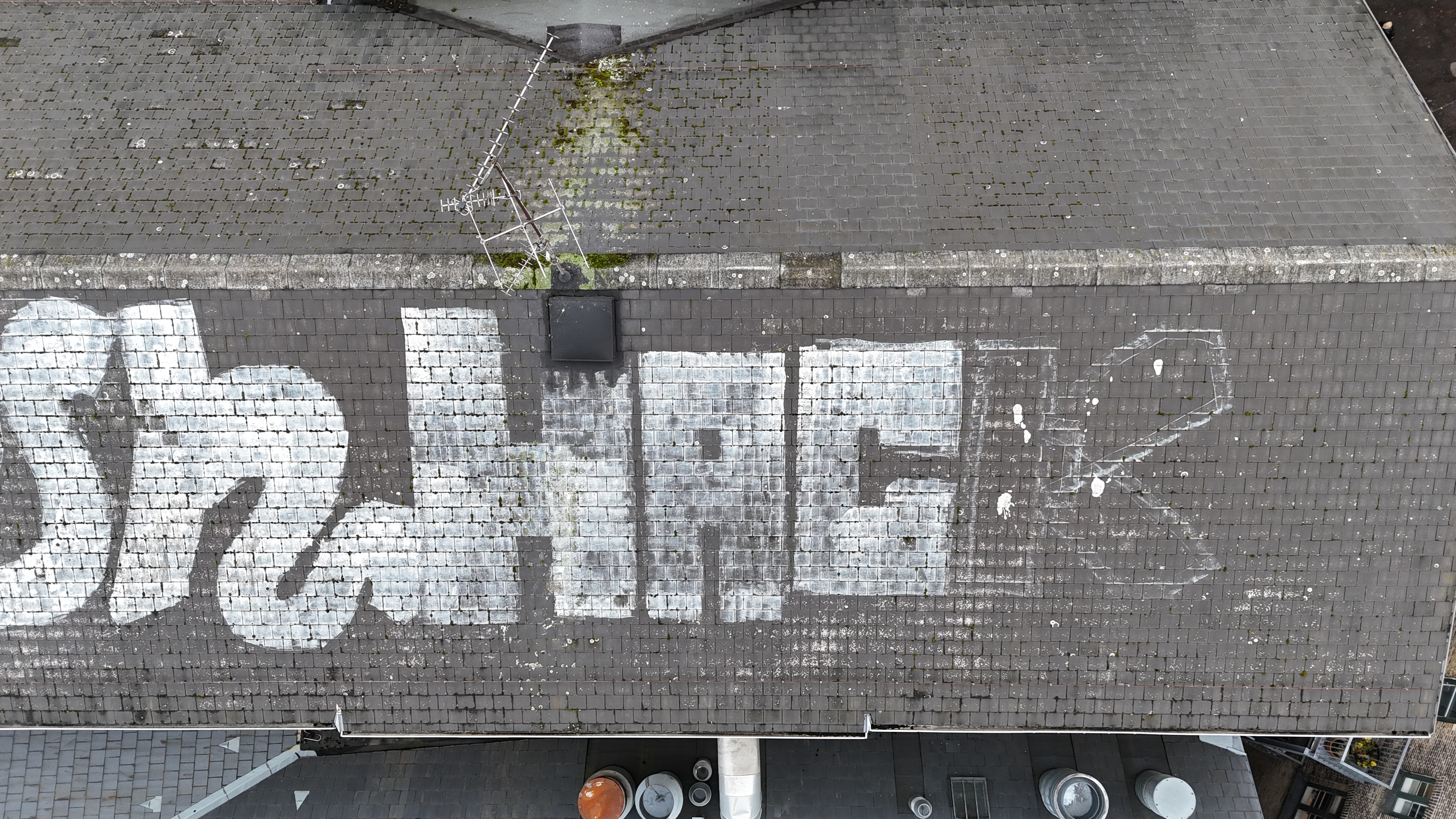 Drone overblik af stor skifertagflade med graffiti-tags og mos langs rygning